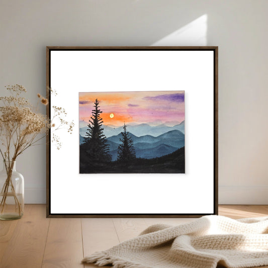 Blue Ridge Sunset paining in a minimal black frame with white matting. Displayed on the floor with beige flowers and a crumpled blanket.