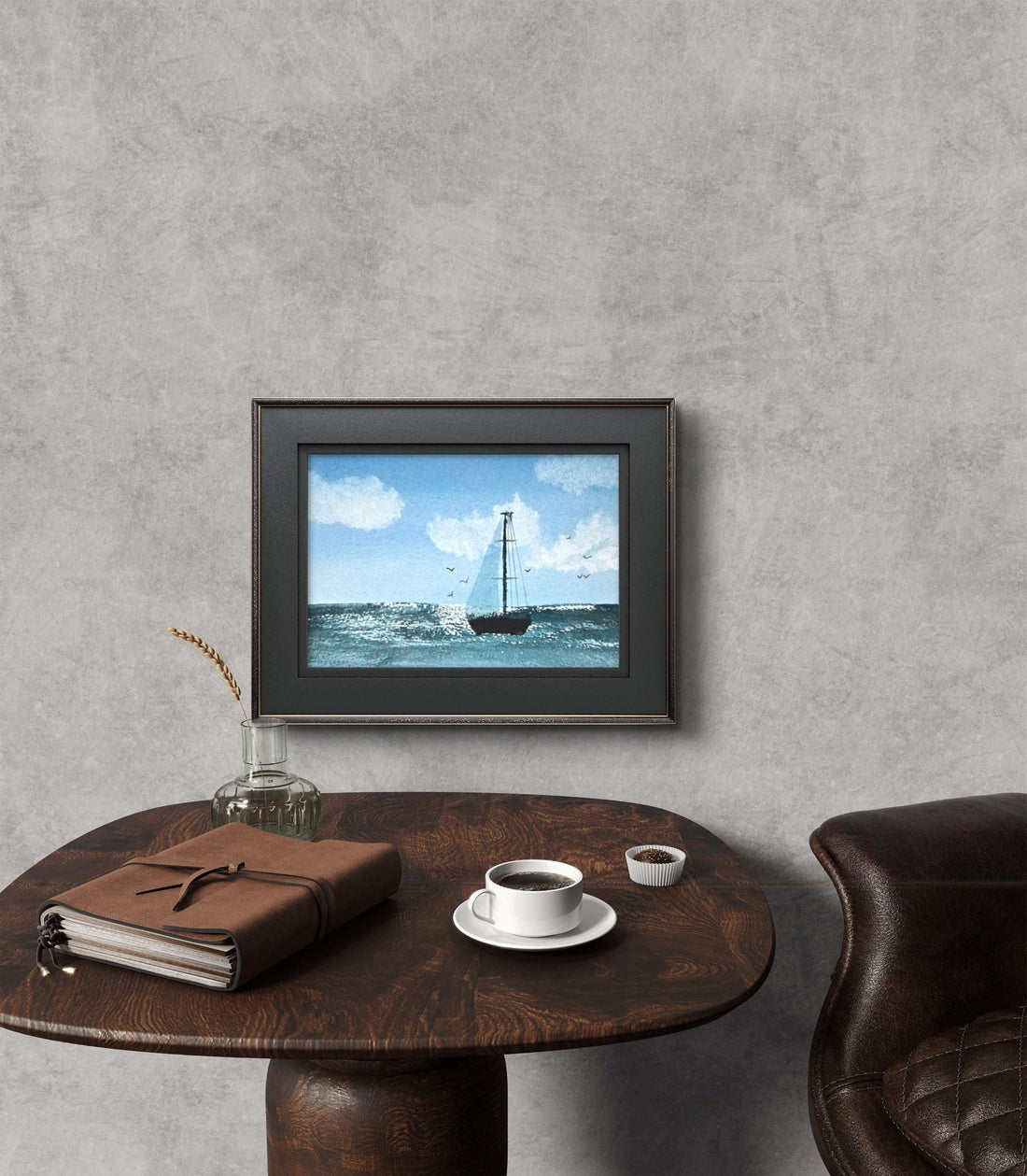 watercolor sailing artwork placed on wall above a brown end table that has a book and coffee on it.
