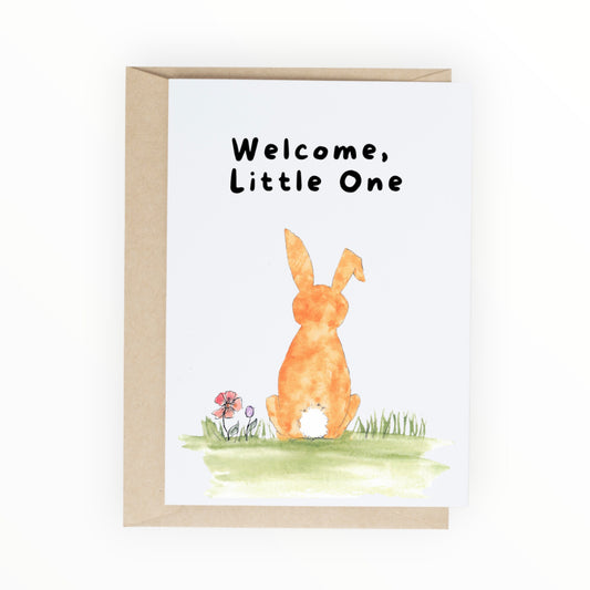 Orange watercolor bunny sitting in grass with the words ‘Welcome, Little One.