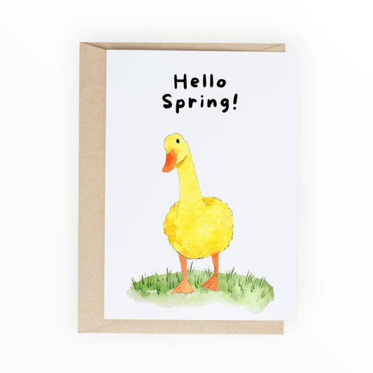 Watercolor yellow duck standing in green grass with text reading ‘Hello Spring.’